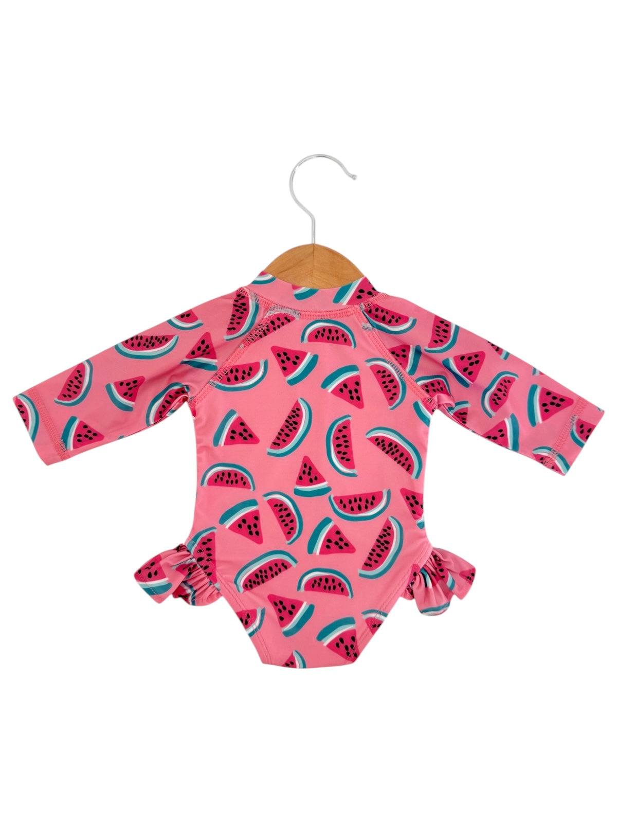Pink long-sleeve swimsuit with a watermelon pattern, featuring ruffles on the sides, hanging on a wooden hanger.