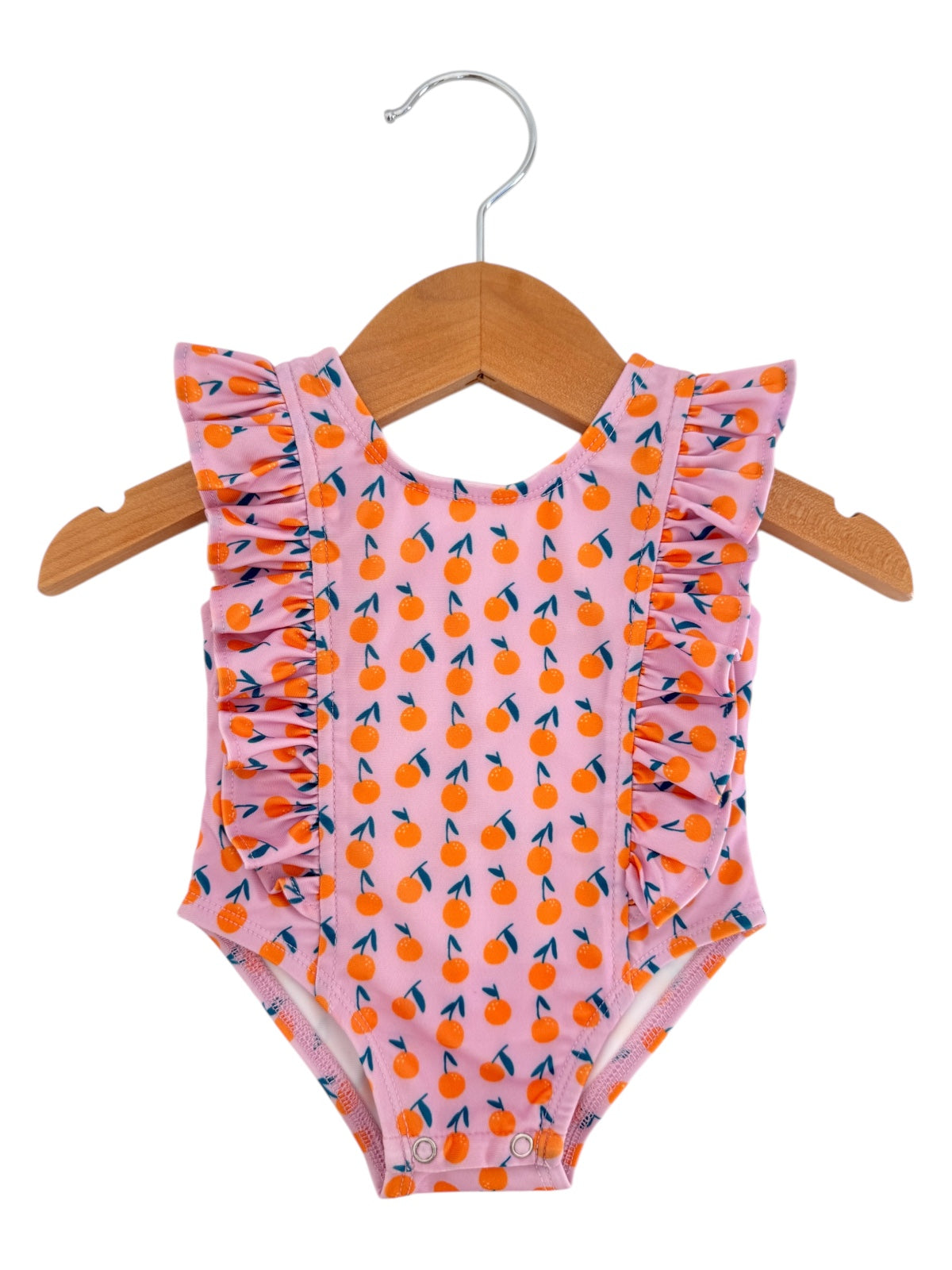 Pink ruffled swimsuit with orange and green fruit pattern hanging on a wooden hanger.