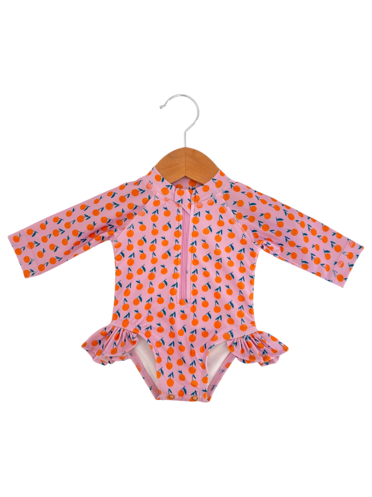 Pink long-sleeve swimsuit with orange fruit design and ruffled edges, hanging on a wooden hanger.