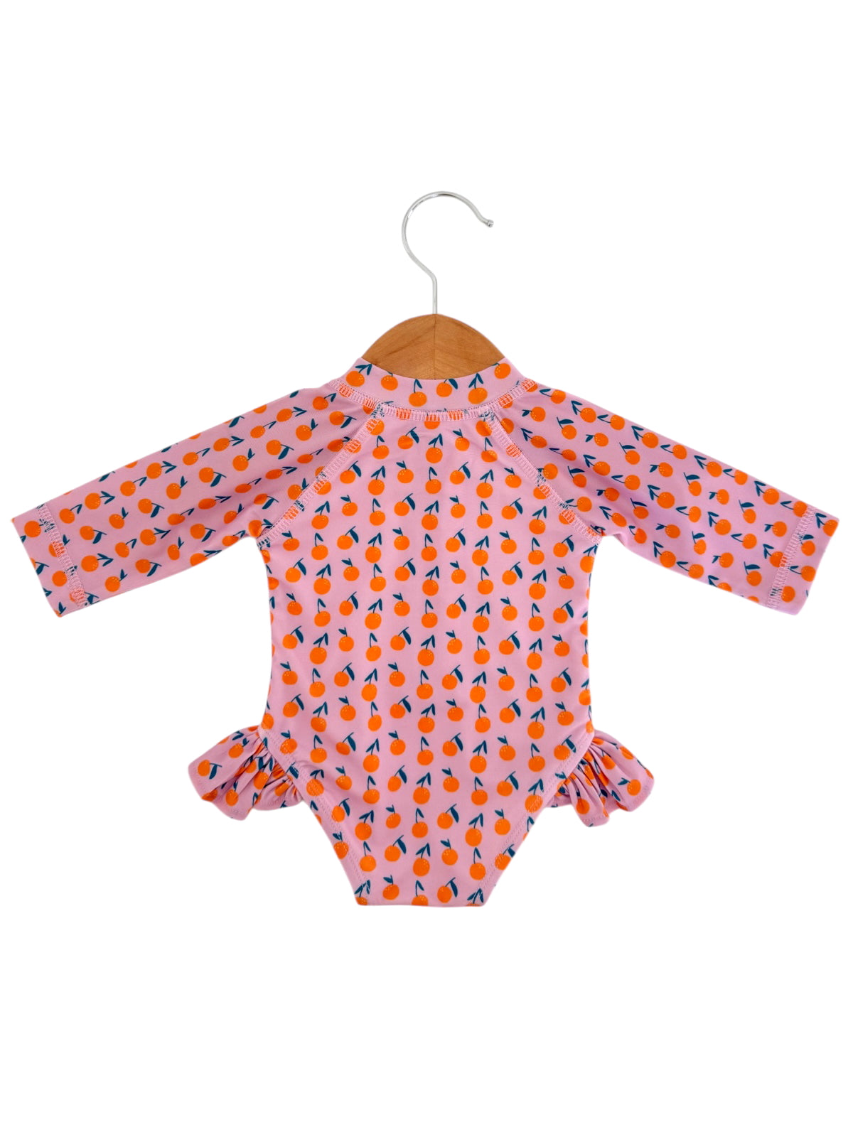 Pink long-sleeve swimsuit with orange fruit pattern, ruffled details, hanging on a wooden hanger.