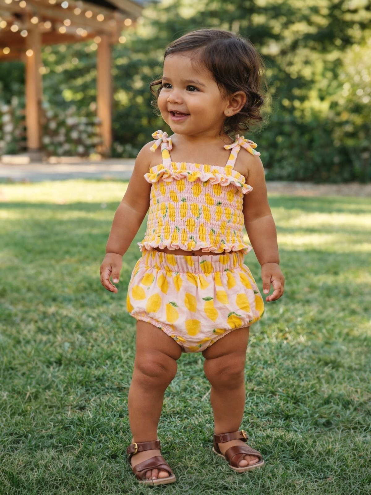 Smiling toddler in a colorful outfit, playing on green grass with a blurred garden background.