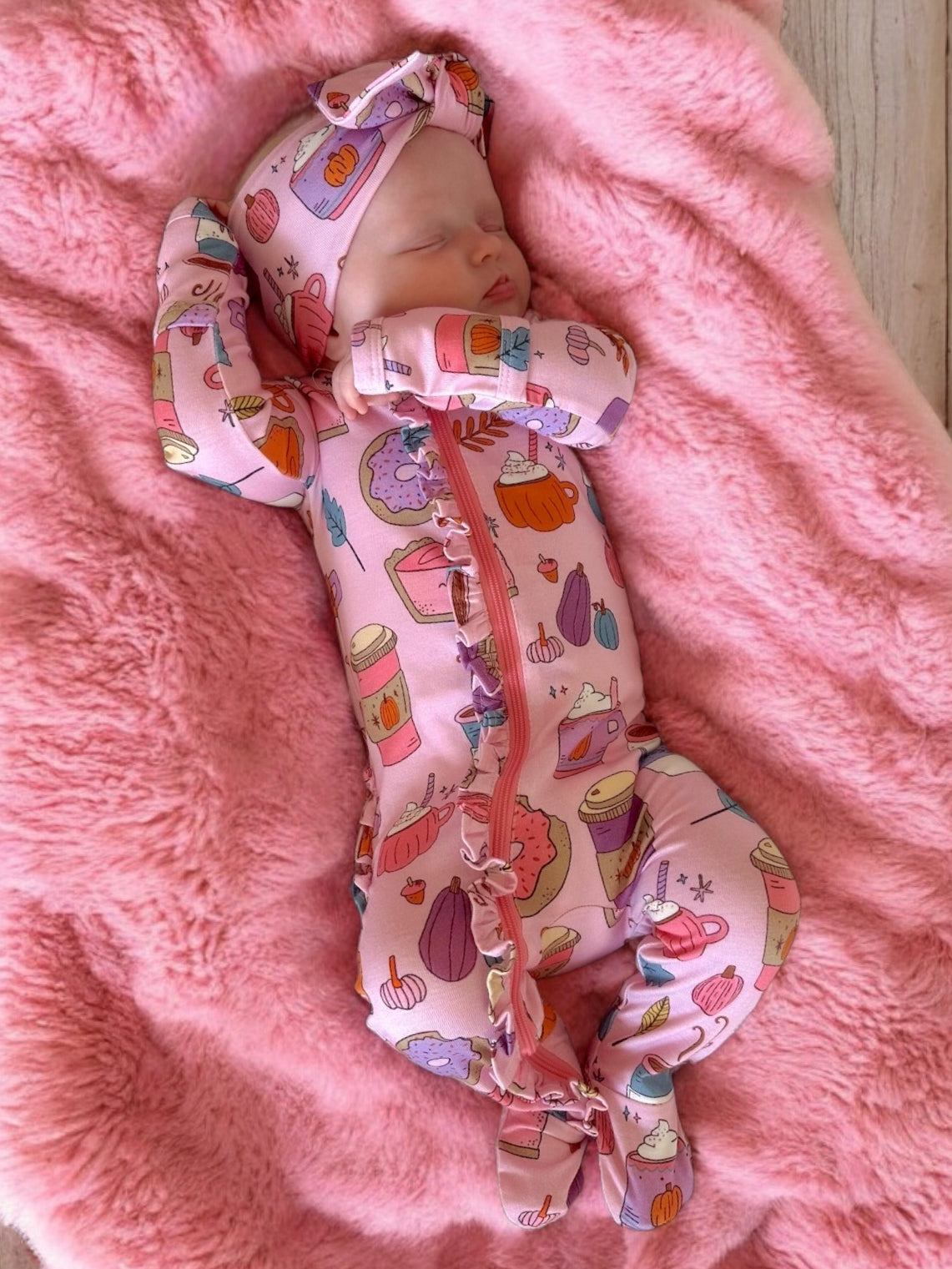 Sleeping baby in pink patterned onesie on a soft pink blanket, surrounded by playful food illustrations.