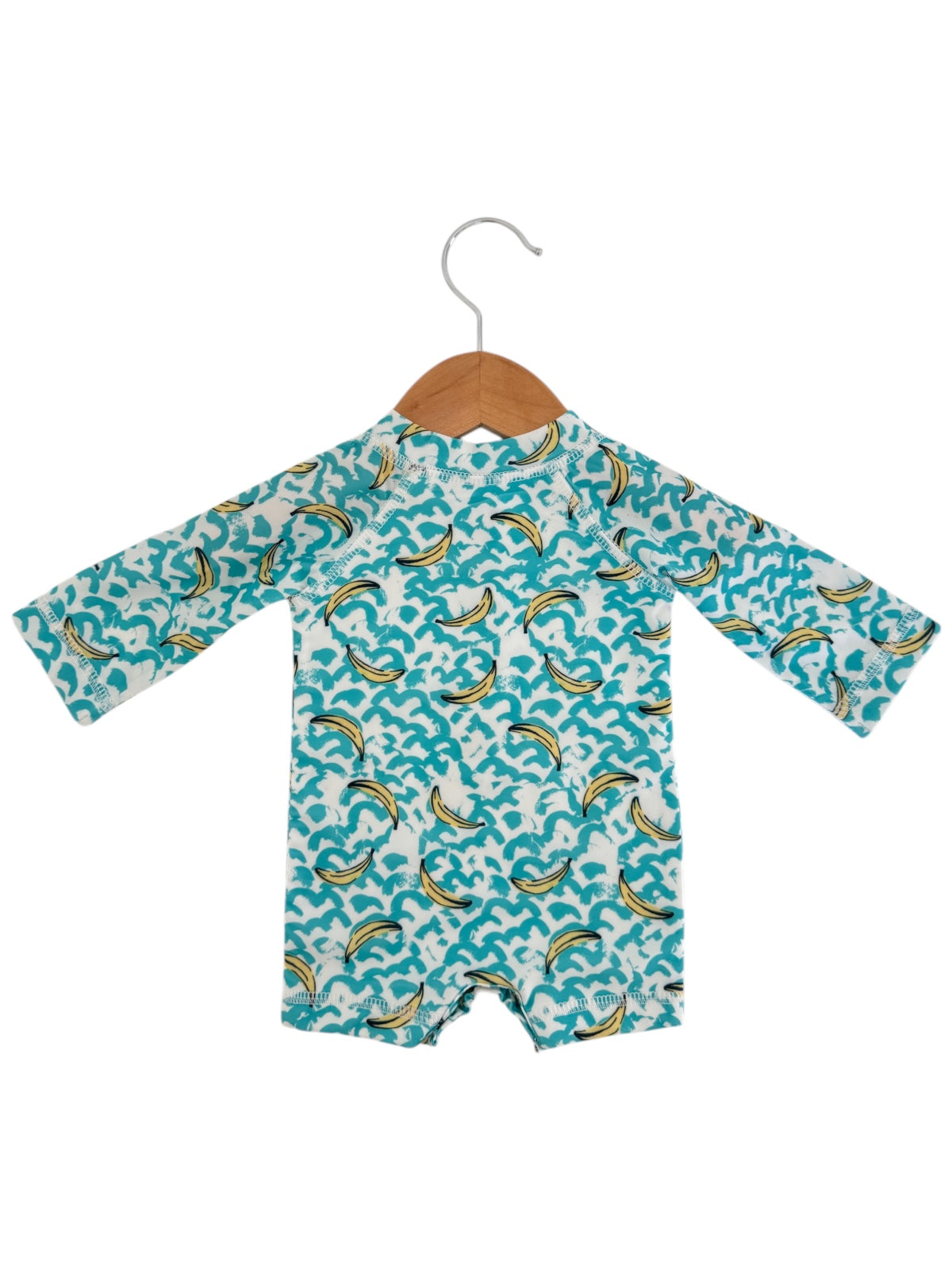 Children's swimsuit hanging on a wooden hanger, featuring a colorful wave and banana pattern.