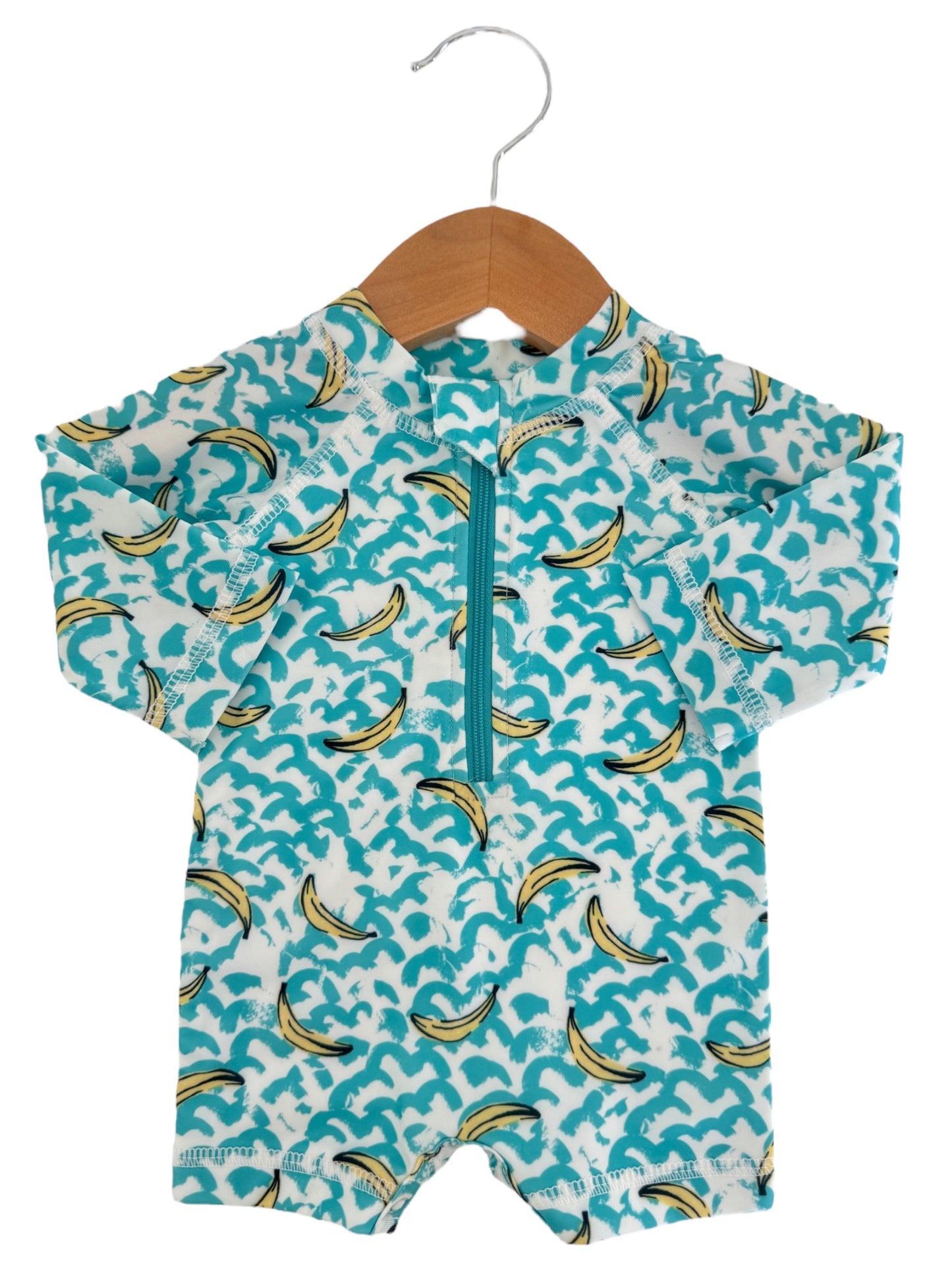 Children's short-sleeve swimsuit with turquoise wave and banana print, displayed on a wooden hanger.