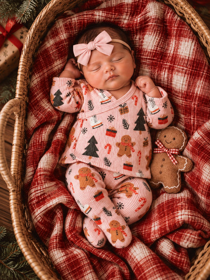 Sleeping baby in festive pajamas, nestled in a cozy basket with a gingerbread plush and a checkered blanket.