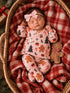 Sleeping baby in festive pajamas, nestled in a cozy basket with a gingerbread plush and a checkered blanket.
