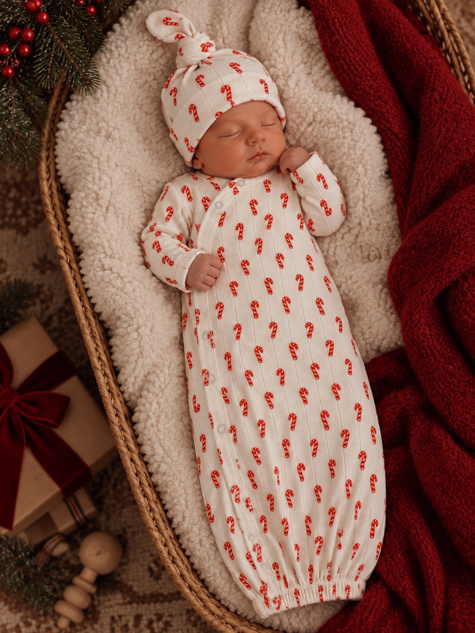 Newborn baby sleeping in a cozy basket, wearing a candy cane-patterned outfit and hat, surrounded by festive decor.