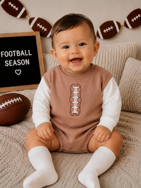 Smiling baby in football-themed outfit, sitting on a cozy blanket near a football and "Football Season" sign.
