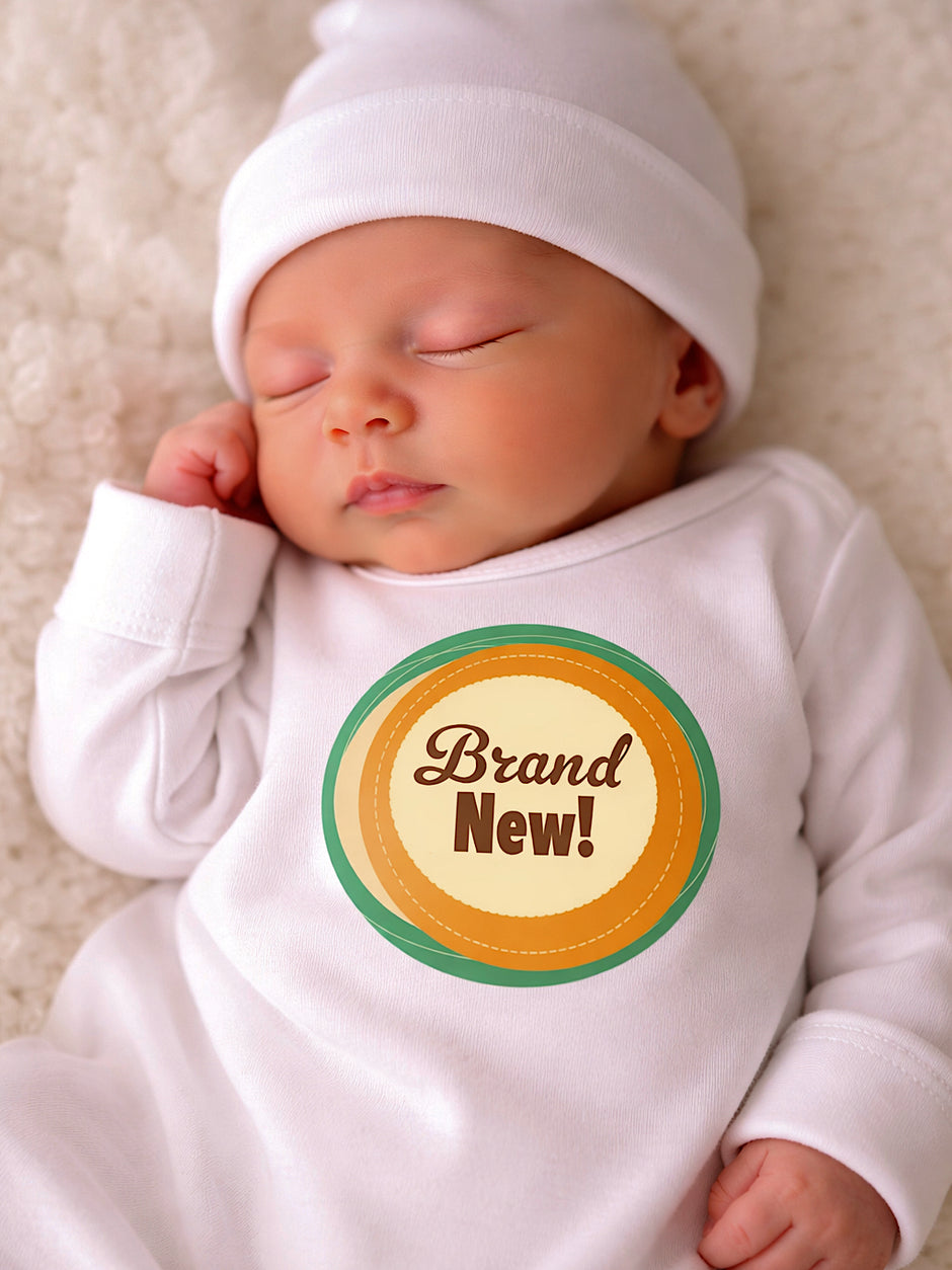 Sleeping baby in a white onesie with a circular "Brand New!" graphic, on a cozy blanket.