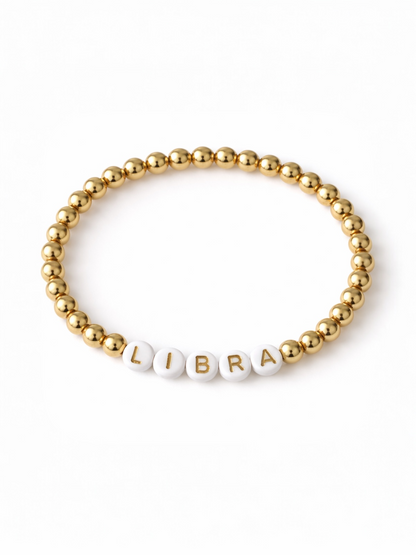 Gold beaded bracelet featuring white letters spelling "LIBRA." Elegant and stylish accessory.