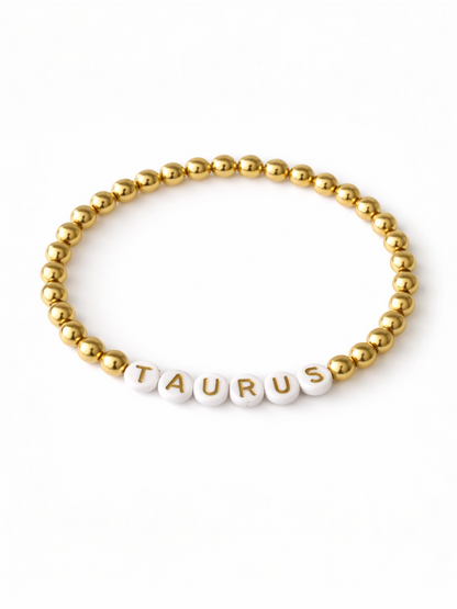 Gold bead bracelet with white letter beads spelling "TAURUS." Perfect for astrology enthusiasts.