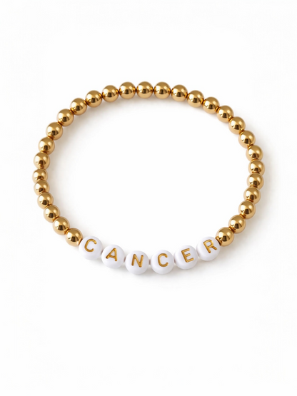 Gold bead bracelet with white letter beads spelling "CANCER." Ideal for awareness and support.
