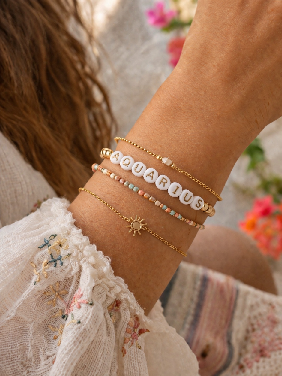 Hand wearing colorful bracelets, including one with "AQUARIUS" letters and a sun charm, against floral background.