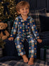 Smiling boy in bear-patterned pajamas, sitting on a cozy blanket near a Christmas tree and plush teddy bear.