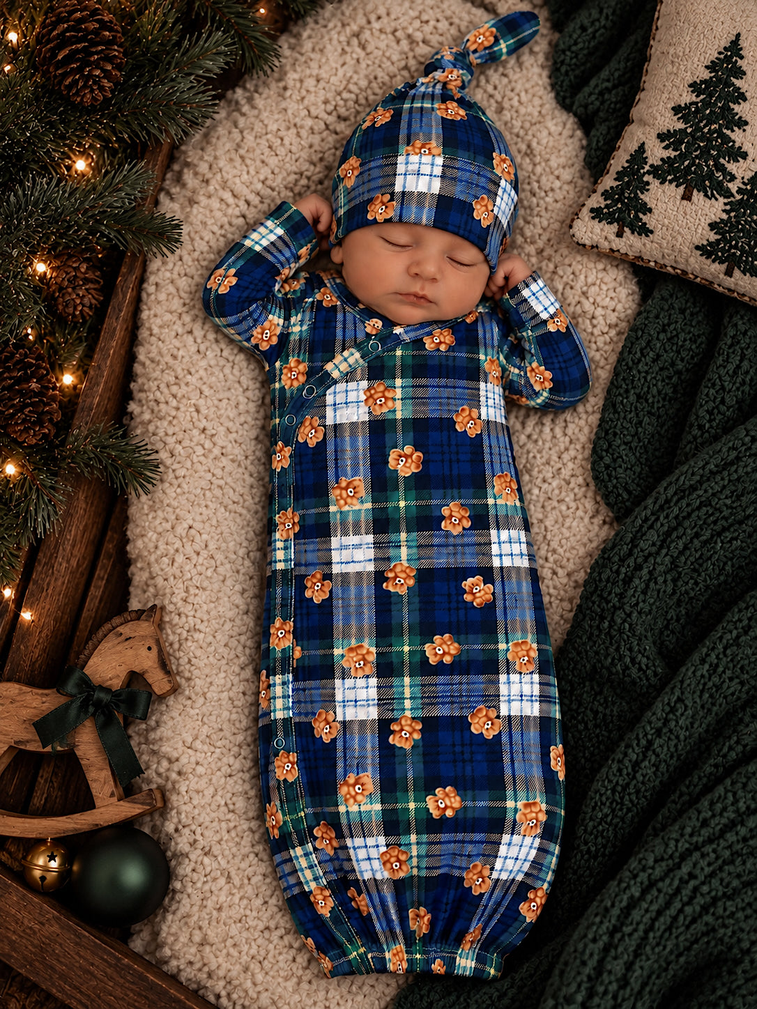 Sleeping baby in a blue plaid outfit with floral patterns, cozy background with greenery and soft textures.