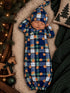 Sleeping baby in a blue plaid outfit with floral patterns, cozy background with greenery and soft textures.