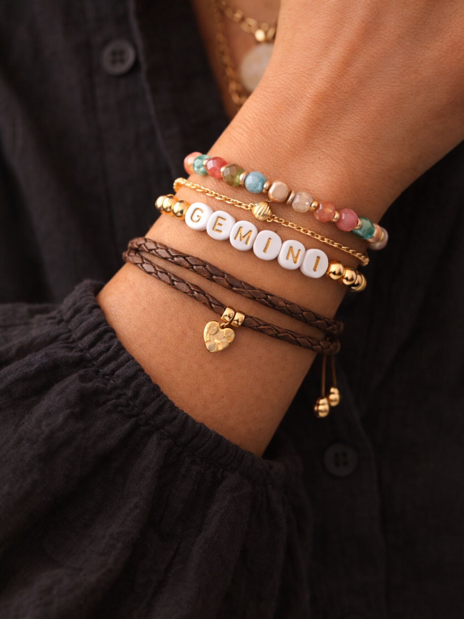 A close-up of a wrist adorned with colorful bracelets, including one with the word "GEMINI" in white beads.