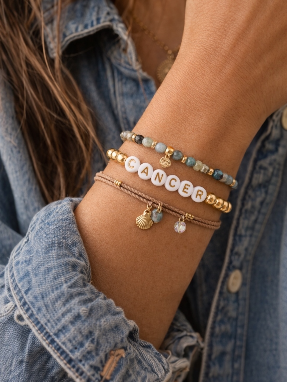 Hand wearing multiple stylish bracelets with the word "CANCER" prominently featured.