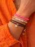 Close-up of a hand wearing stacked bracelets, including pink beads, gold accents, and an "Aries" charm.