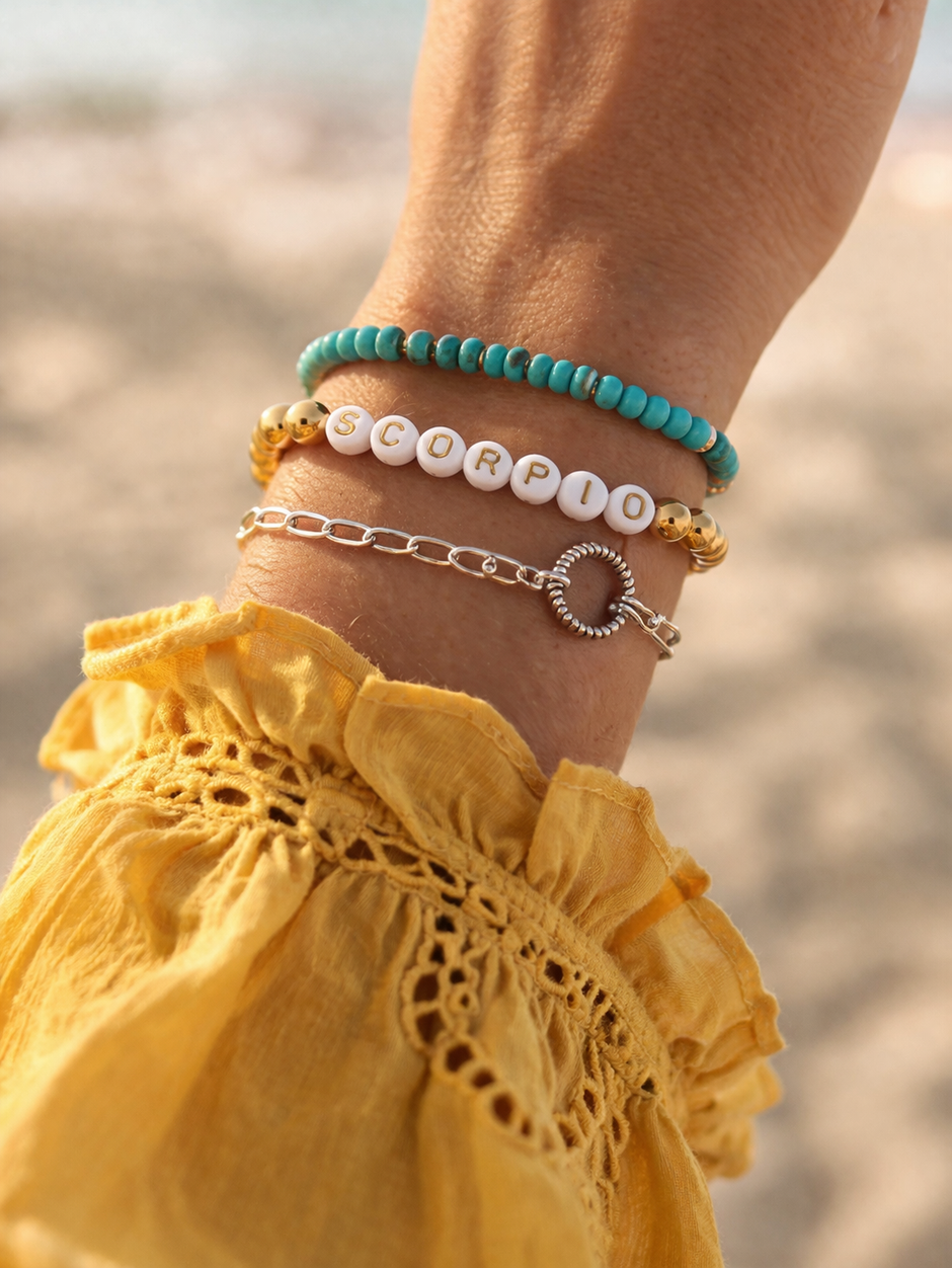 Two colorful bracelets adorn a wrist, featuring a white bead bracelet with "SCORPIO" text.