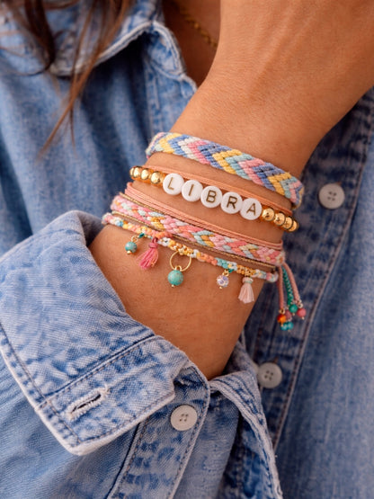Colorful bracelets on a wrist, featuring beads, charm details, and "LIBRA" letters, against a blue denim shirt.