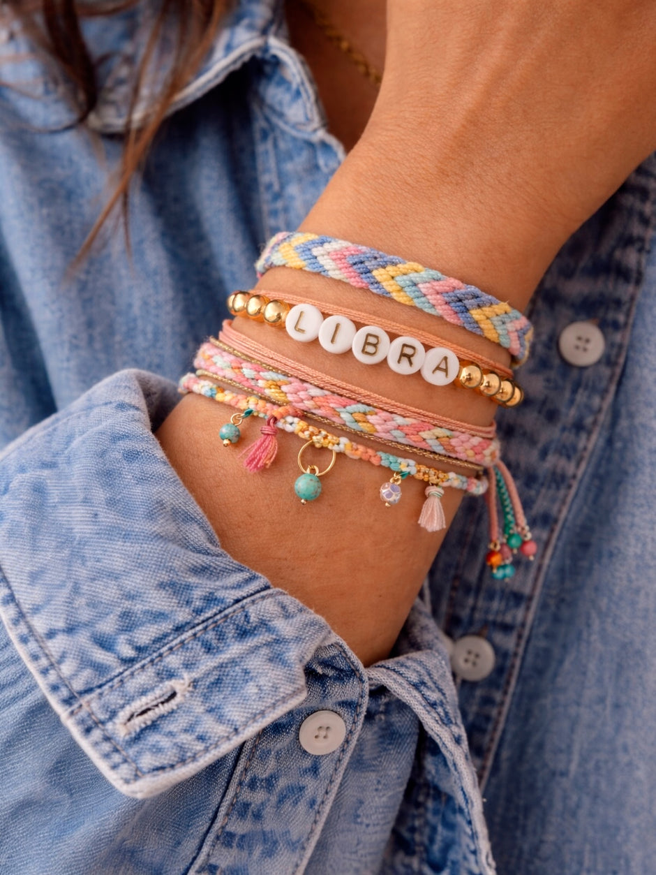 Colorful bracelets on a wrist, featuring beads, charm details, and "LIBRA" letters, against a blue denim shirt.
