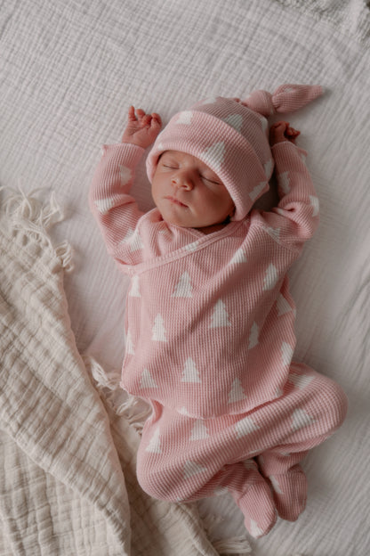 Newborn baby in pink outfit with white patterns, resting peacefully on a soft blanket.