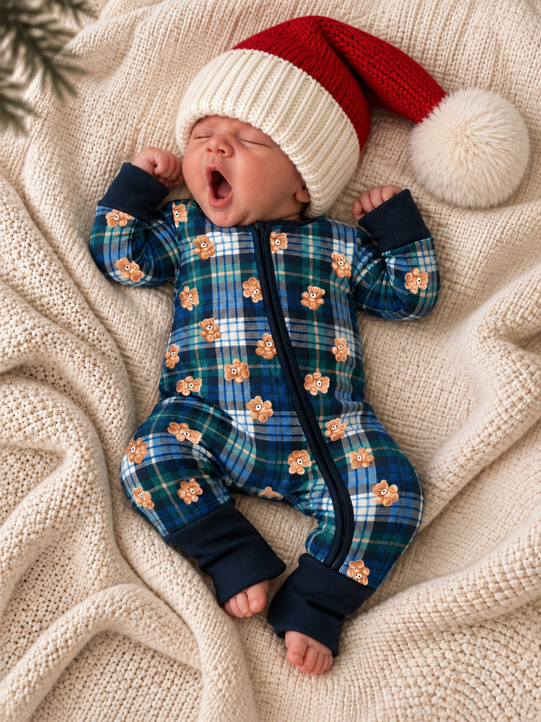 Baby in plaid onesie and a festive red and white hat yawns on a cozy blanket.