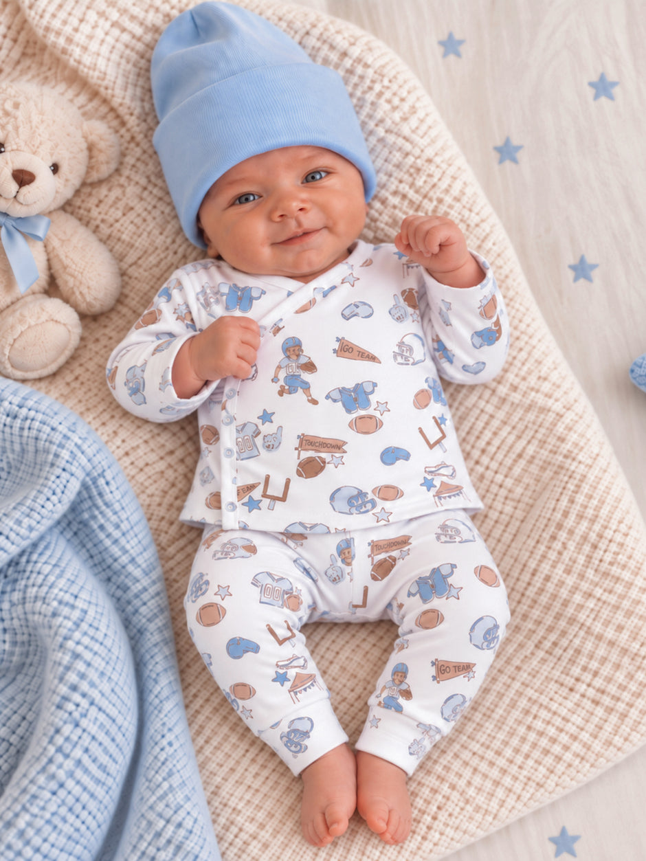 Smiling baby in a blue hat and sports-themed outfit, surrounded by plush toys and soft blankets.