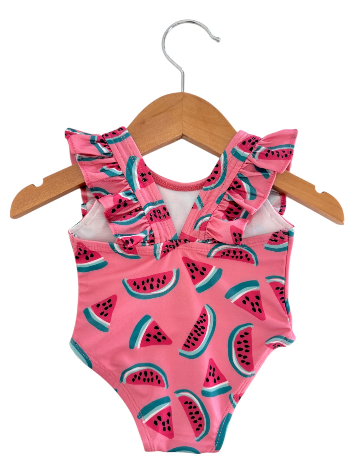 Pink swimsuit with a watermelon print and ruffled shoulders, hanging on a wooden hanger against a white background.
