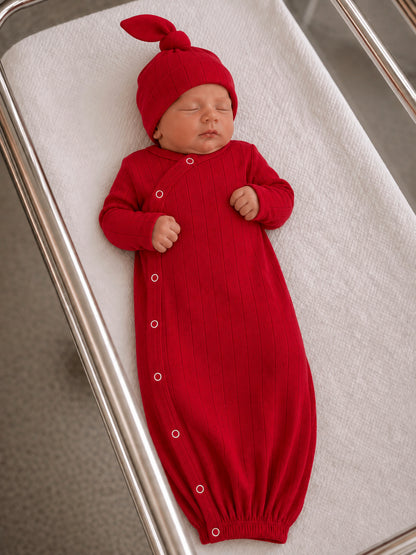 Newborn sleeping in a red ribbed outfit and matching hat, resting on a white swaddling blanket.