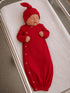 Newborn sleeping in a red ribbed outfit and matching hat, resting on a white swaddling blanket.