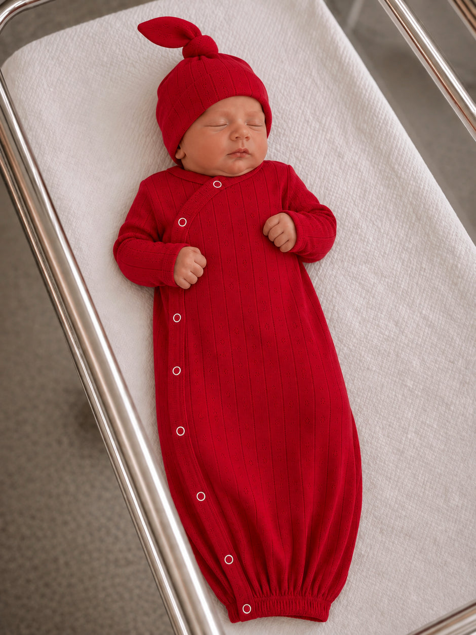 Newborn sleeping in a red ribbed outfit and matching hat, resting on a white swaddling blanket.