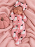 Baby girl in pink ghost-patterned onesie and matching headband, resting on a pink blanket with a pumpkin.