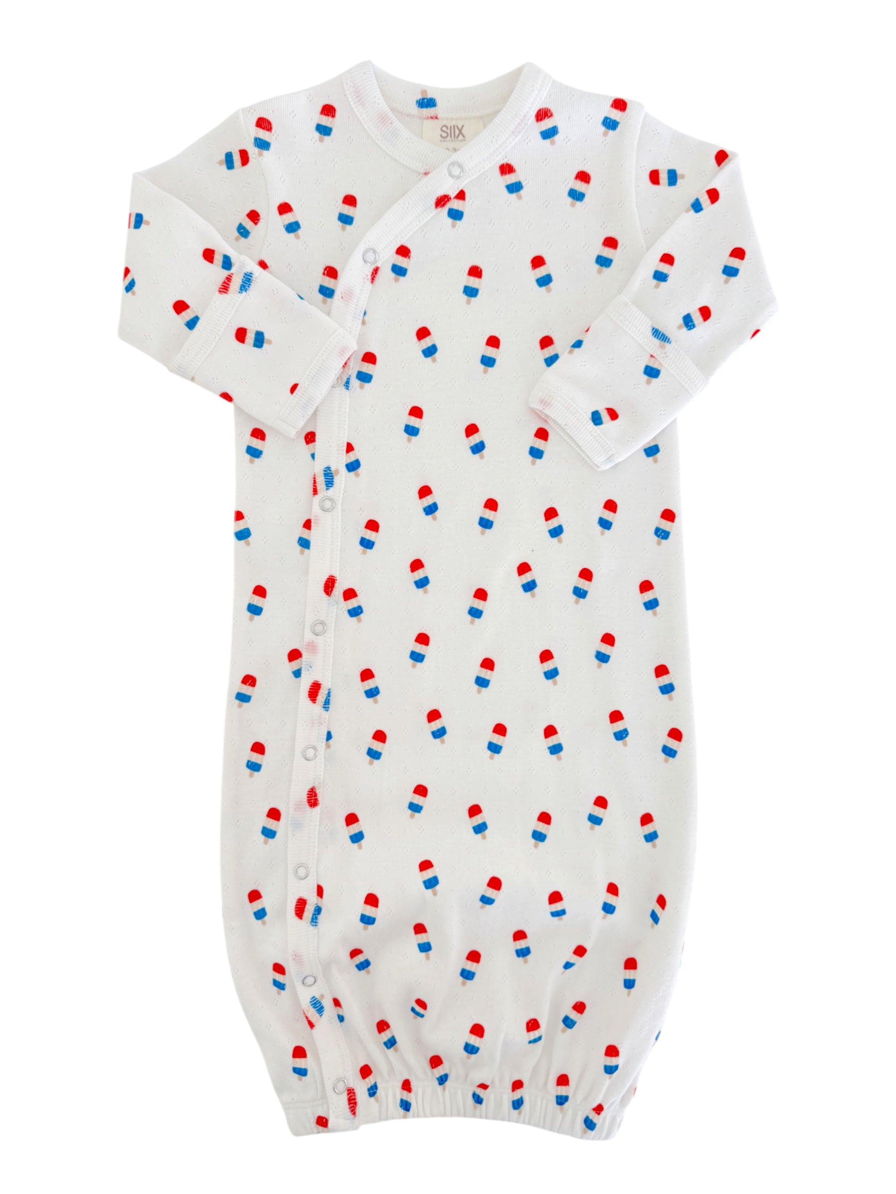 White baby gown with red and blue pill patterns, featuring long sleeves and snap buttons down the side.
