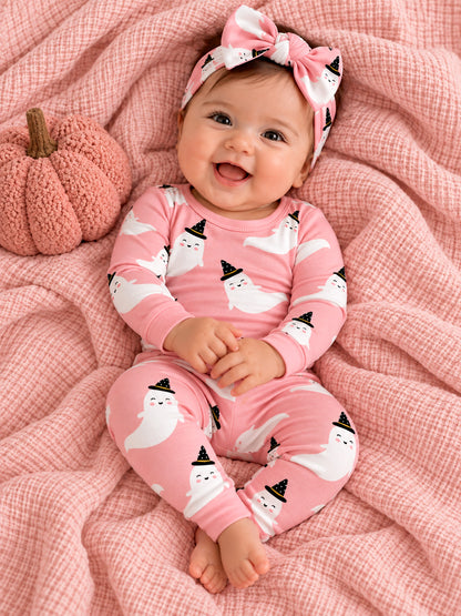 Smiling baby in pink ghost-themed pajamas sits on a soft blanket with a pumpkin, wearing a matching headband.