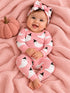 Smiling baby in pink ghost-themed pajamas sits on a soft blanket with a pumpkin, wearing a matching headband.