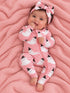 Smiling baby in a pink ghost-printed onesie and bow, lying on a pink blanket.