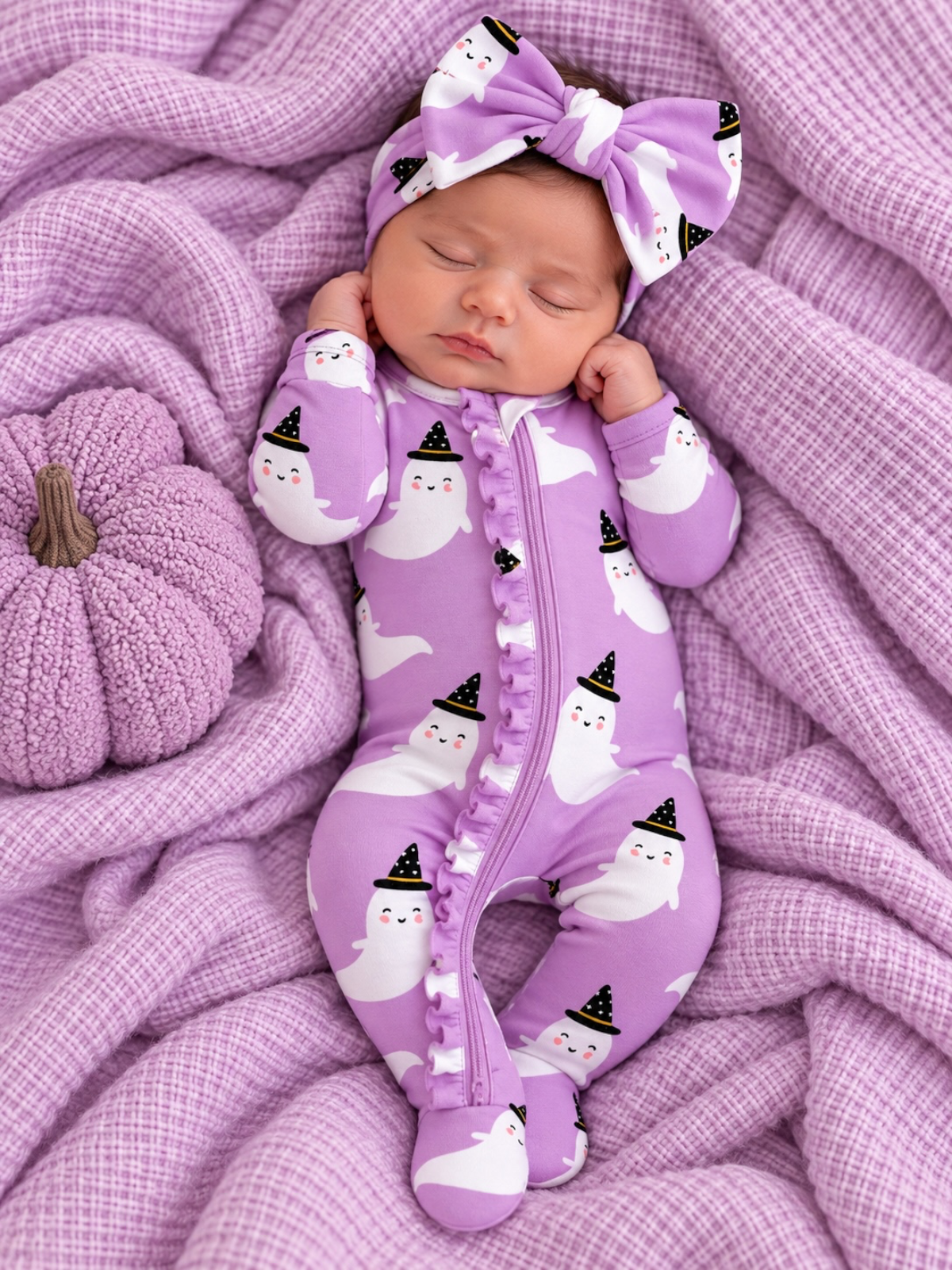 Baby girl in a purple ghost-patterned outfit and headband, resting on a soft, textured lavender blanket.
