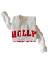 White sweater with red "HOLLY" lettering, styled with a ribbed texture and rolled sleeves.