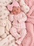 Newborn baby girl in a pink floral outfit with a large bow, sleeping beside a plush bunny on a floral blanket.