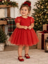 Smiling toddler in a festive red dress with a bow, surrounded by Christmas decorations and gifts.