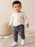 Toddler in lightning-patterned shirt and gray joggers, smiling while standing on a wooden floor.