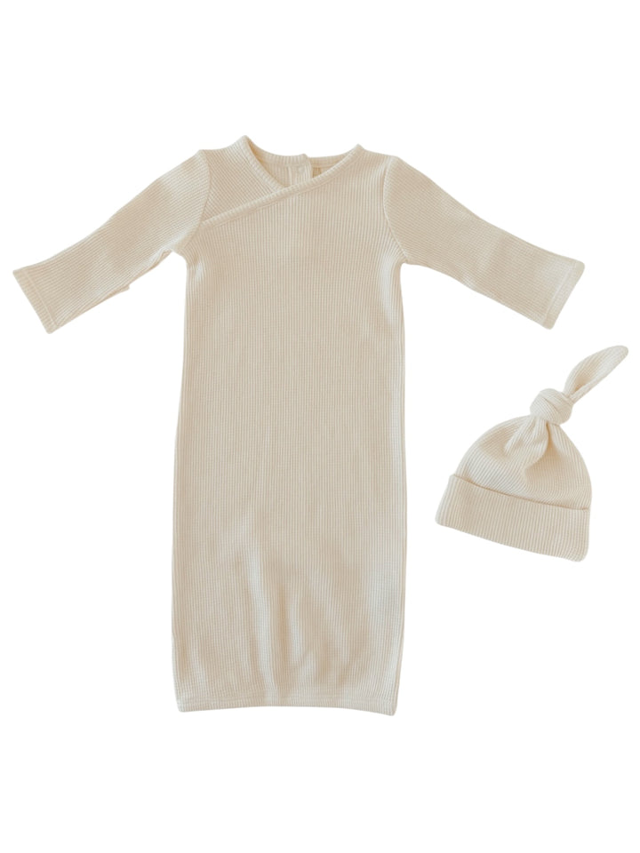 Light beige infant gown and matching knotted hat on a white background, perfect for newborns.