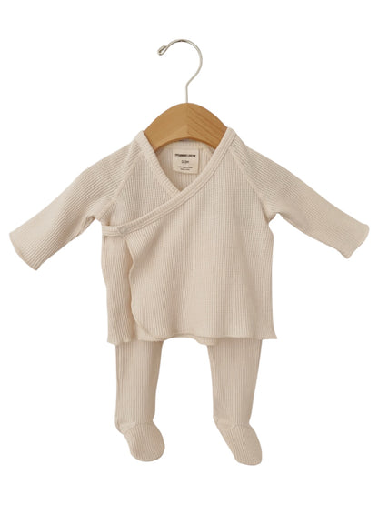 Cream-colored infant outfit with long sleeves and pants, displayed on a wooden hanger.