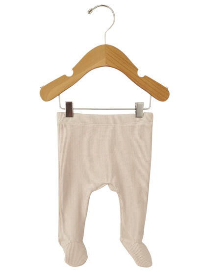 Pale beige baby leggings hanging on a wooden hanger against a white background.