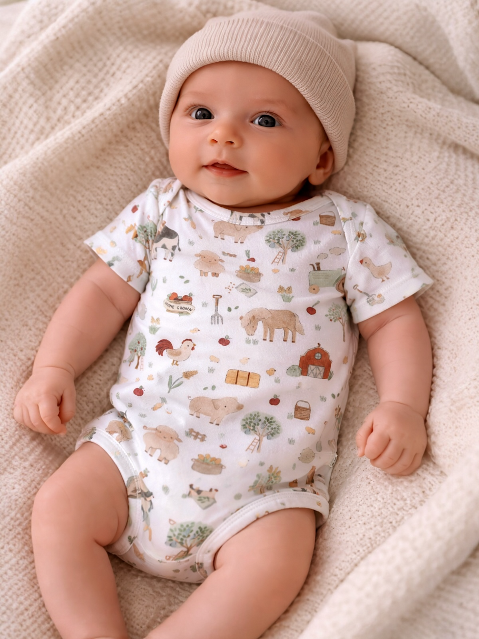 Smiling baby in a light-colored onesie with animal prints, wearing a beige hat, resting on a textured blanket.