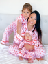 Mother and two daughters in matching pink pajamas with candy cane print, smiling together on a white bed.