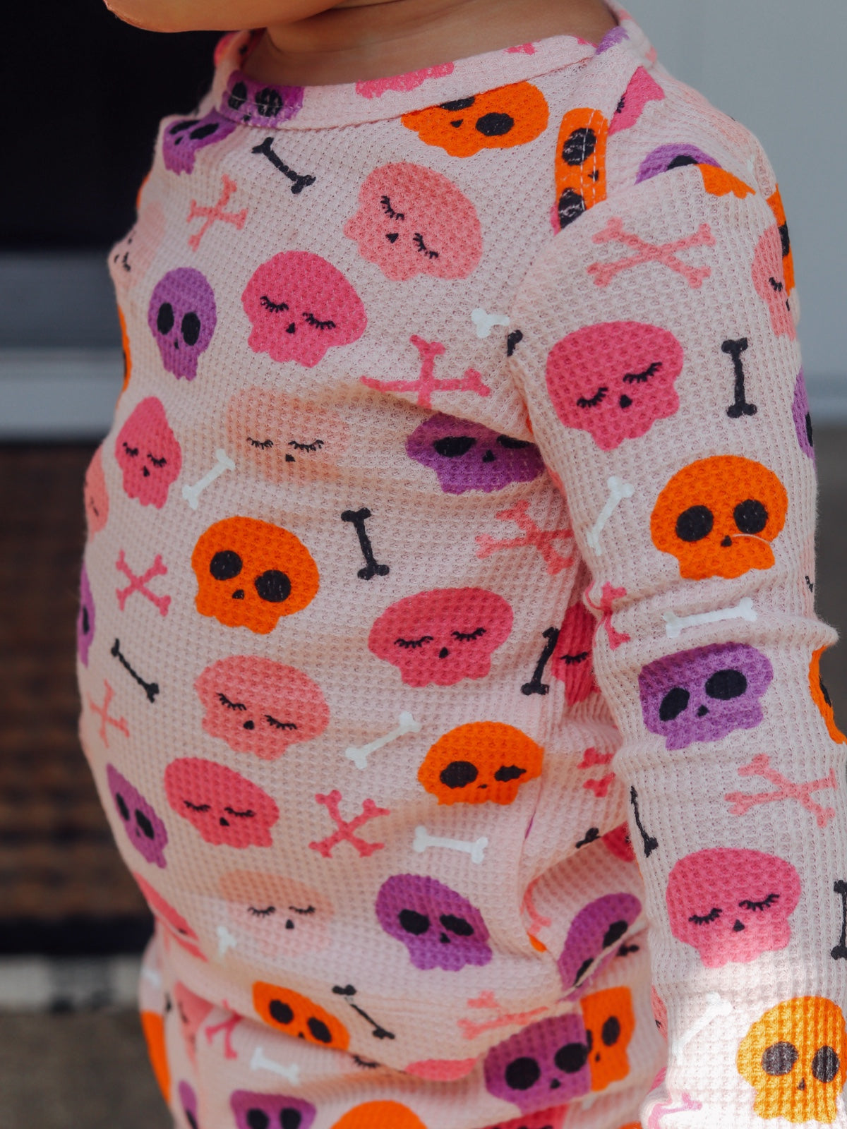Child wearing a pink outfit with colorful skull and bone patterns, smiling and looking to the side.