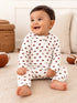 Baby sitting on a rug, smiling, wearing a white outfit with football prints, surrounded by footballs.